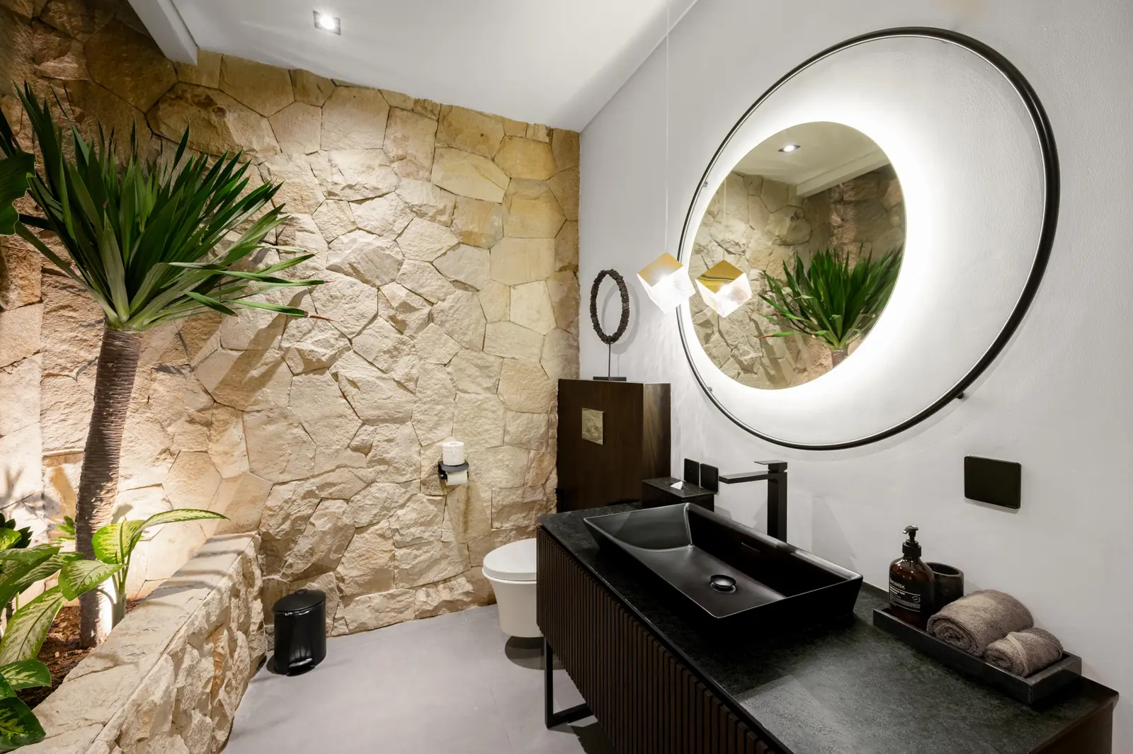 Guest bathroom on the living room level with natural stone wall, indoor palm and round backlit mirror MAR Bali 1 Pererenan Bali